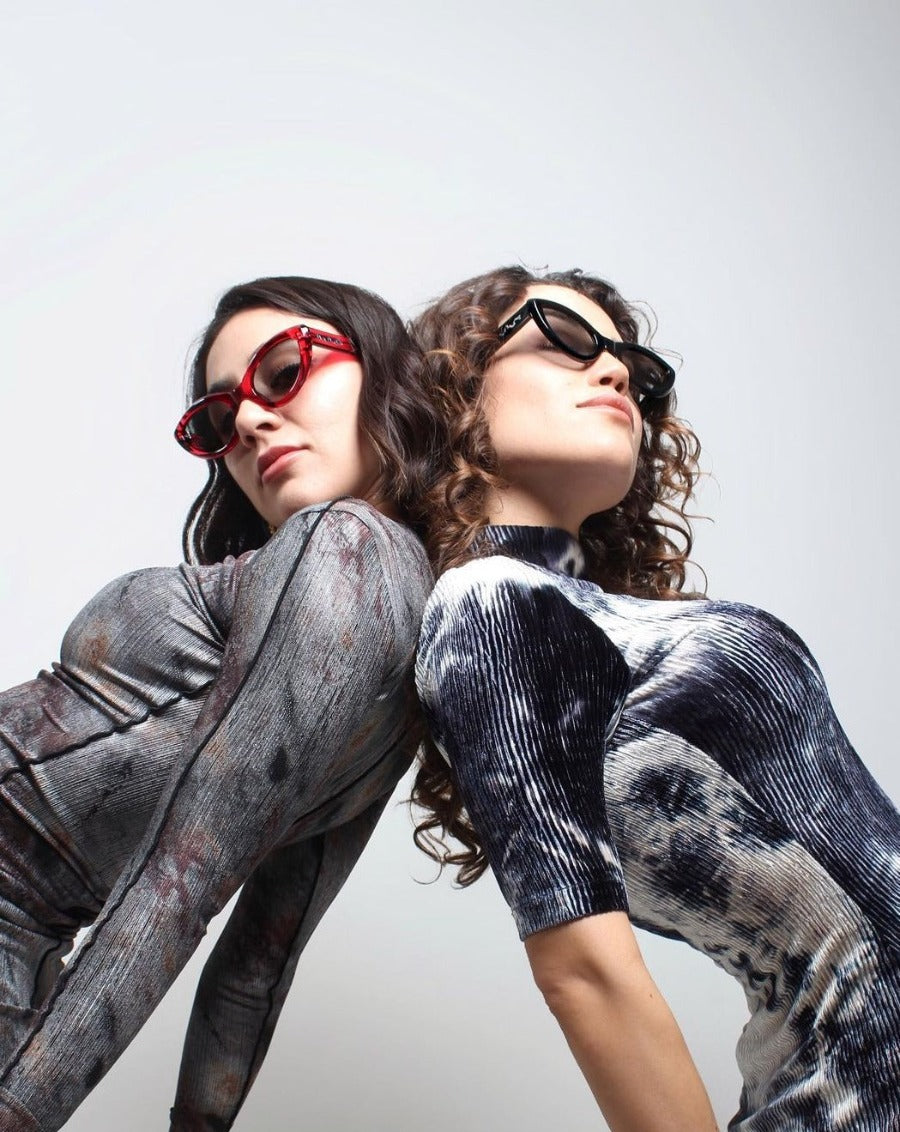 Futuristic models posing back to back while wearing spacial dresses and scribble dot sunglasses 