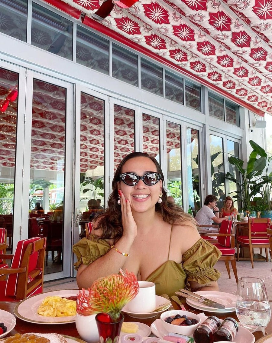 Woman posing looking happy at a restaurant, touching her face while wearing scribble dot sunglasses